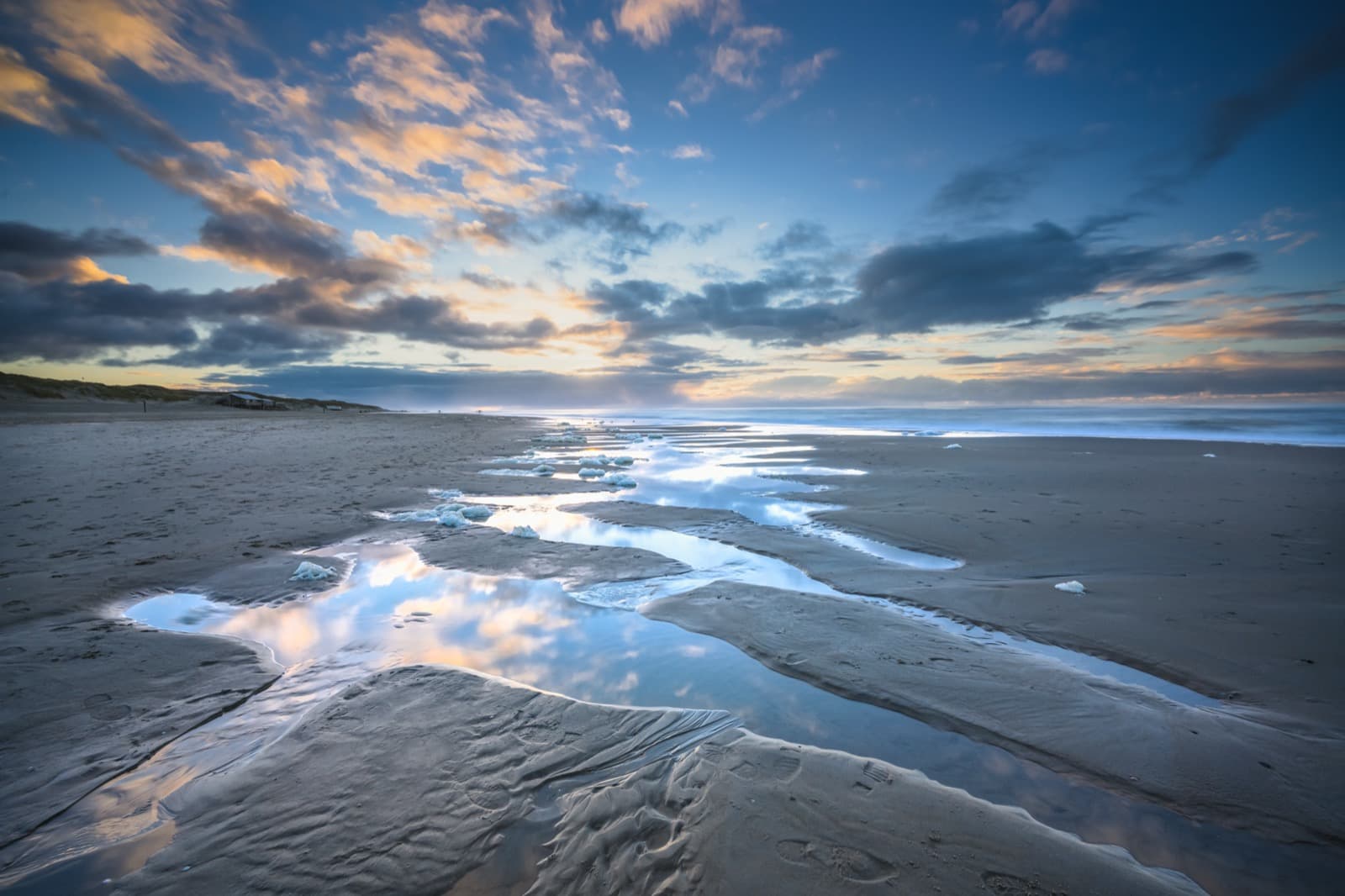 Tide pools reflecting the sky on a calm beach at dusk